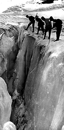 Quatre alpinistes regardent au-dessus d’une crevasse.